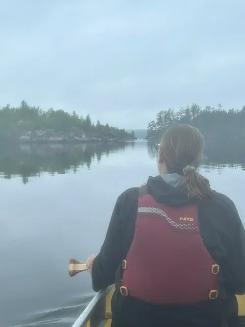 A canoeist resting on a quiet lake surrounded by trees